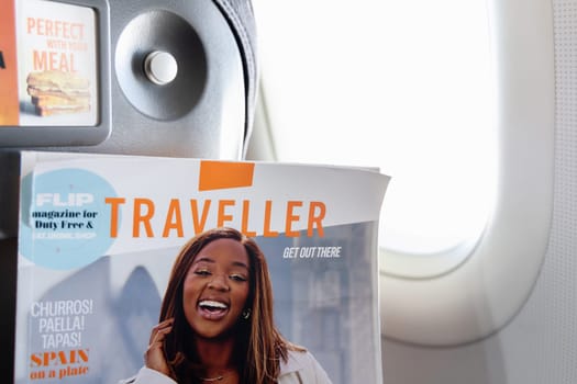 Female hands holding the magazine Traveller on board an airplane. Paris, France - January 6, 2025