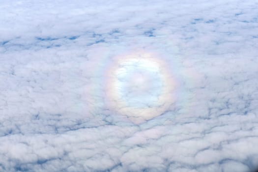 Round rainbow in the cloudy sky. View from the airplane window.