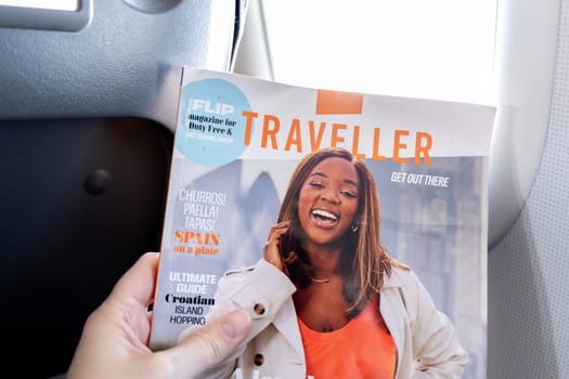 Female hands holding the magazine Traveller on board an airplane. Paris, France - January 6, 2025