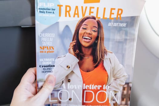 Female hands holding the magazine Traveller on board an airplane. Paris, France - January 6, 2025