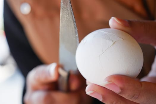A detailed closeup shot captures a hand firmly holding a cracked egg with a knife