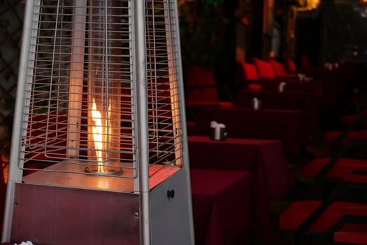 A patio heater is glowing warmly amidst empty tables, inviting a sense of comfort and warmth