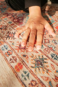 A graceful hand gently resting upon a beautifully designed and intricately patterned carpet