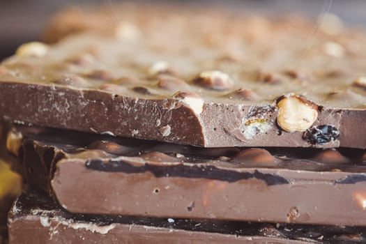 A closeup view of multiple stacked chocolate bars artfully arranged with crunchy nuts on top