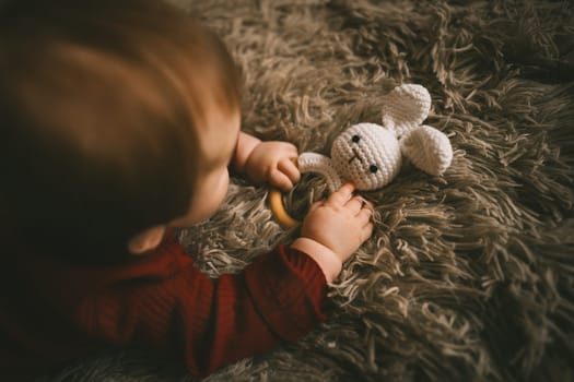 Adorable baby playing with bunny toy on fluffy brown bed coat. Babyhood and playtime concept. High quality photo