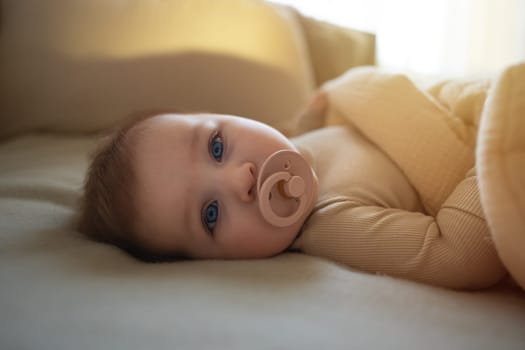 Beautiful baby girl in white clothes with soother lying in bed. Adorable kid portrait. 5 month old child. High quality photo