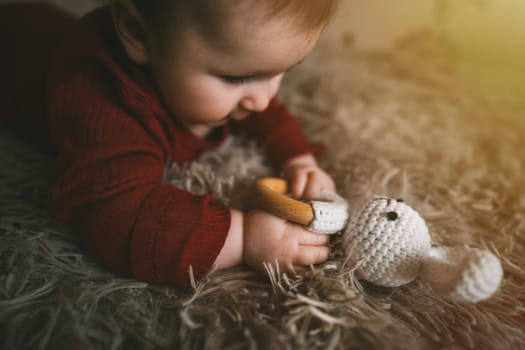 Adorable baby playing with bunny toy on fluffy brown bed coat. Babyhood and playtime concept. High quality photo