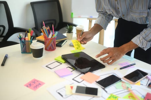 Team of creatives collaborating on a UX UI project at workspace filled with flowcharts and digital prototypes.