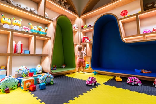 Toddler exploring a modern playroom filled with colorful toys, shelves, and cushioned seating areas