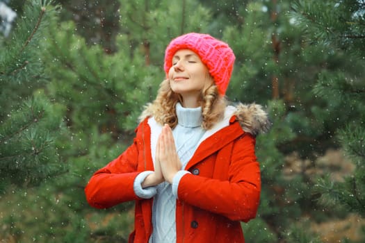 Calm relaxed healthy young woman meditates in winter forest, girl practicing doing yoga exercises outdoors in park against Christmas tree, snow, nature background, warm weather