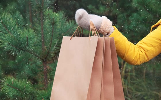 Purchase, holidays, female hand holding showing paper shopping bags, gift against Christmas tree background