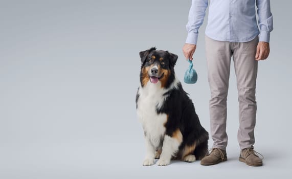 Pet owner holding a full dog poop bag, his dog is sitting next to him, pet care and hygiene concept
