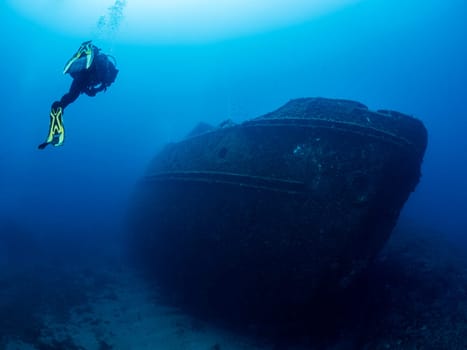 scuba diver diving near of the wreck of an old ruined ship on the bottom of deep blue sea with clear water and light glare, concept of underwater adventure and seascape