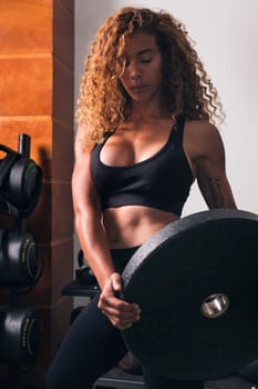 concentrated muscular sportswoman standing with heavy weight plate during workout in gym, concept of fitness and active lifestyle