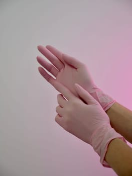 Female cosmetologist nurse wearing pink close-up medical gloves on white background, vertical, slow motion