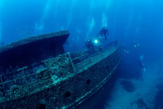group of scuba divers diving near of the wreck of an old ruined ship on the bottom of deep blue sea with clear water and light glare, concept of underwater adventure and seascape