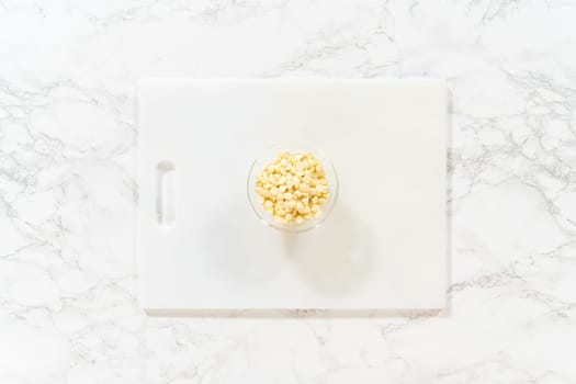Flat lay. On a white cutting board, skillfully chopping white chocolate chips with a knife adds the perfect touch to a baking adventure.