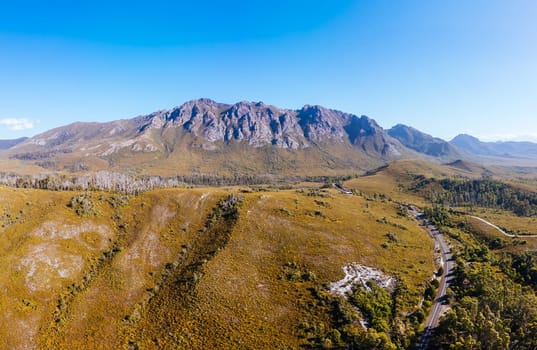 An aerial view of Gordon River Rd at the Sentinel range of mountains near Bitumen Bones Sculpture on a hot summer's afternoon in Southwest National Park, Tasmania, Australia