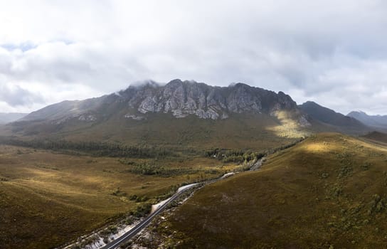 An aerial view of Gordon River Rd at the Sentinel range of mountains near Bitumen Bones Sculpture on a hot summer's afternoon in Southwest National Park, Tasmania, Australia