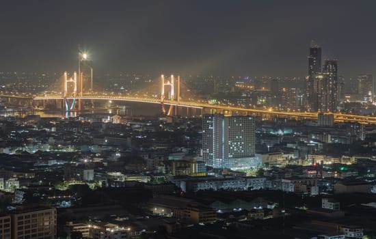 Bangkok, Thailand 31 Dec, 2024 - Nightscape view of Skyscrapers with Thotsamarachan Bridge (Rama IX Bridge) crossing Chao phraya river. Beautiful city of Bangkok with bright glowing lights, use it as your Wallpaper, Poster and Space for text, Selective focus.