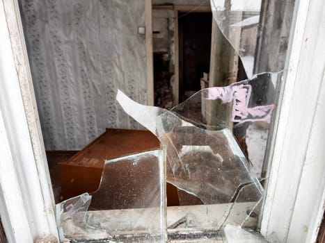 The broken glass of a window reveals an abandoned interior, with scattered debris hinting at past occupancy and neglect.