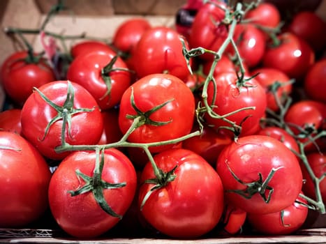 Vibrant red tomatoes are piled in a wooden box at an outdoor market, showcasing their freshness and ripe quality under sunlight.