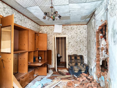 Interior of a once-cozy home shows decay with broken walls, scattered debris, and worn-out furniture in an abandoned state.