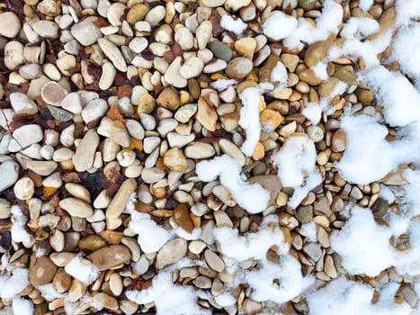Pebbles of various sizes and colors are scattered across a surface, partially covered with a thin layer of snow, evoking a peaceful outdoor ambiance.