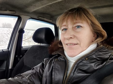 A mature woman enjoying her adventure trip, taking a selfie in her car while surrounded by a snowy landscape and a sense of wanderlust.