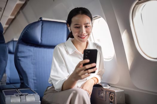 A businesswoman uses her smartphone while traveling on a plane, showcasing modern work flexibility and in-flight productivity.