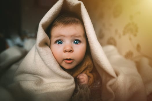Blue-eyed baby girl crawling on bed under the blanket. Adorable kid portrait. 5 month old child. Childhood concept. High quality photo
