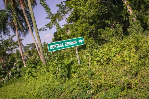 Green road sign indicating the direction to montana redonda amidst tropical vegetation in the dominican republic