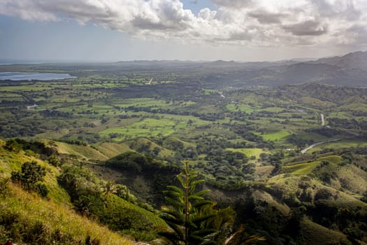 Scenic landscape showcasing the beauty of nature in the dominican republic, featuring rolling green hills, distant mountains, and a glimpse of the ocean