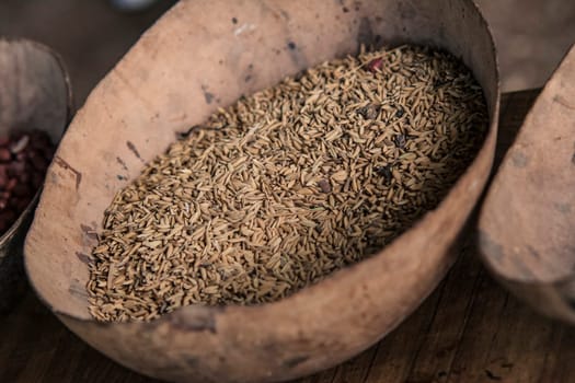 Dry rice grains displayed in a rustic wooden bowl on a wooden surface