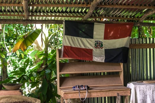 Dominican flag hanging in a rustic wooden shack surrounded by lush tropical vegetation in montana redonda, dominican republic