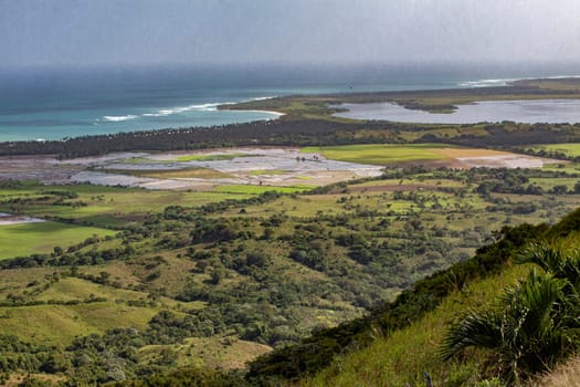 Breathtaking scenery unfolds in the dominican republic, showcasing rolling green hills, vast fields, and the glistening coastline under a dramatic sky