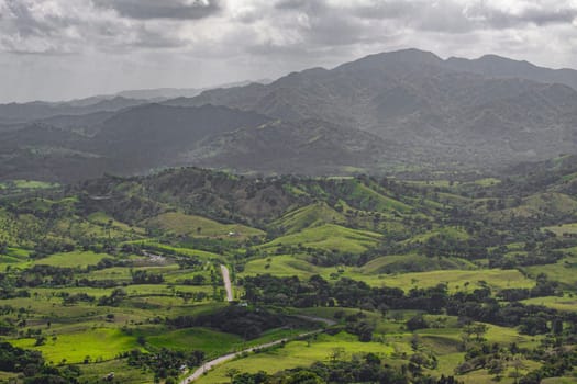 Scenic view of a winding road traversing a vibrant green valley amidst rolling hills and distant mountains in montana redonda, dominican republic