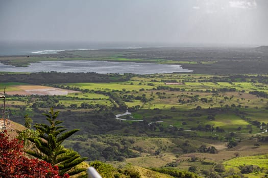 Scenic vista from montana redonda in the dominican republic, featuring a river meandering through verdant fields, with the ocean in the distance