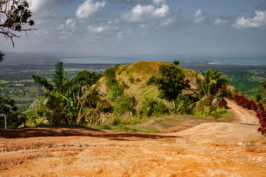 Lush vegetation and red dirt road leading to scenic overlook with ocean and valley views in montana redonda, miches, dominican republic