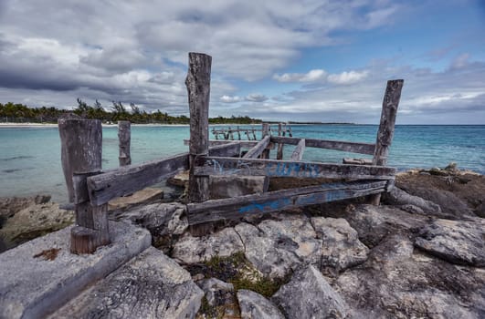 Decaying wooden pier structure sinking into the rocky shore of xpu-ha beach in riviera maya, mexico, under cloudy sky