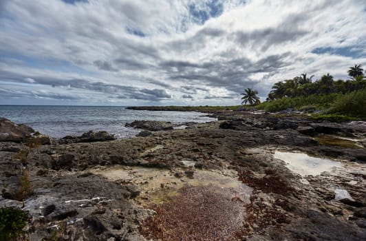 Breathtaking scenery of the rocky coastline in xpu-ha, mexico, where the turquoise waters meet the shore under a cloudy sky