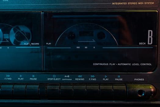 Close-up of a vintage cassette deck playing a tape, illuminated by blue light, showcasing the controls and display