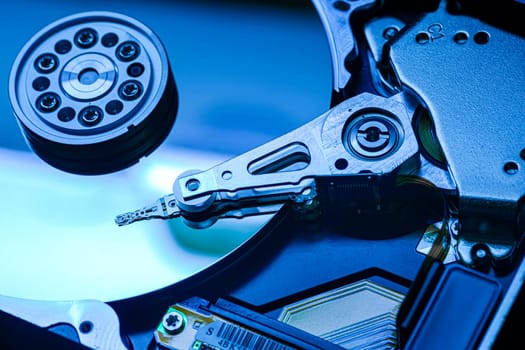 Close-up of hard disk drive internals bathed in blue light, showcasing read/write head actively scanning the platter
