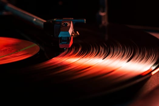 Close-up of a record player needle playing a vinyl record with a red light effect, creating motion blur