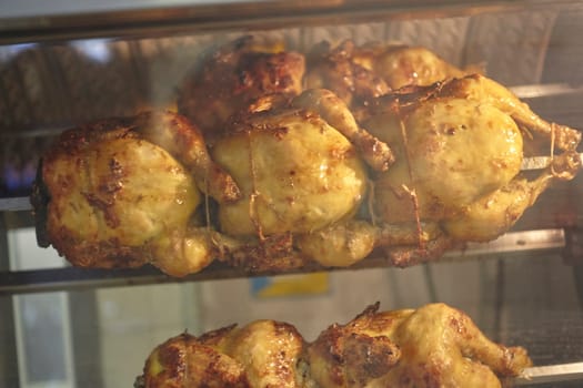 Delicious rotisserie chicken cooking on a spit in a commercial oven, rotating slowly and becoming golden brown