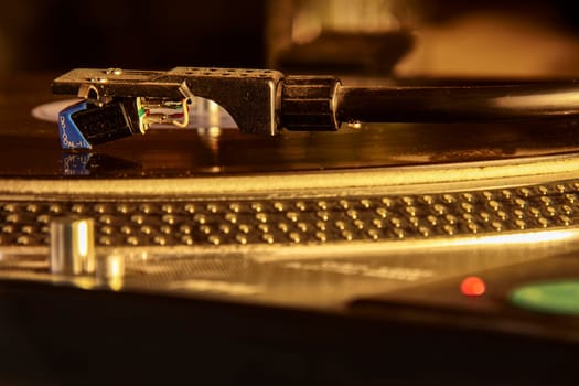 Close-up of a turntable needle playing a vinyl record, illuminated by warm light