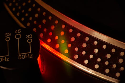 Close-up of a turntable speed selector, bathed in red and green light, creating a vibrant and dynamic atmosphere