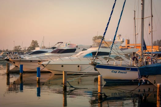 Yachts and sailboats are gently swaying alongside a dock in the serene atmosphere of a marina at sunrise