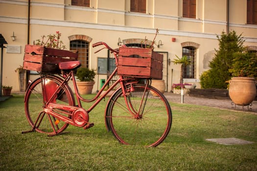 Red vintage bicycle with wooden baskets parked on grass in front of a building, creating a charming rustic scene