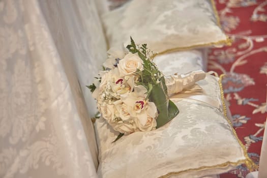 White roses and orchids wedding bouquet lying on a silk kneeler, ready for the ceremony